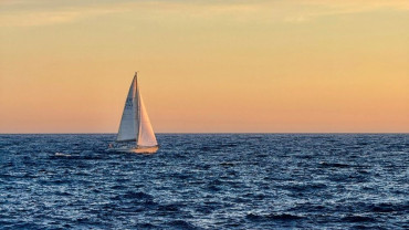 Small sailboat on calm water at sunset, symbolizing adventure and humor in aging