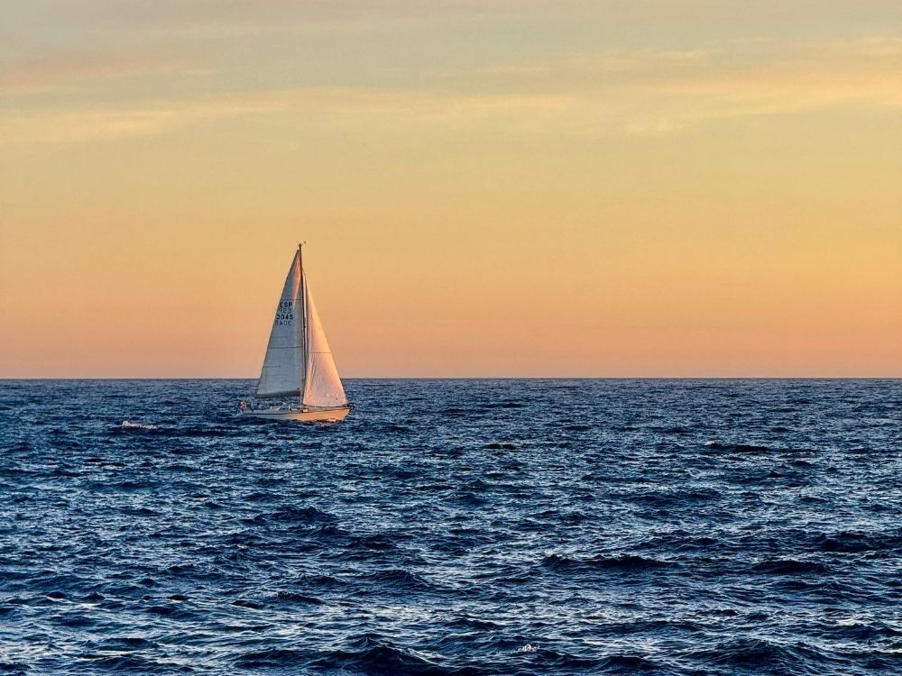 Small sailboat on calm water at sunset, symbolizing adventure and humor in aging