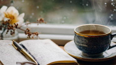 Steaming cup beside an open journal with a pen, set on a windowsill, symbolizing reflection and daily practice