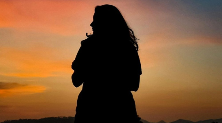 Silhouette of person meditating on a mountain top at sunset, symbolizing transition and reflection