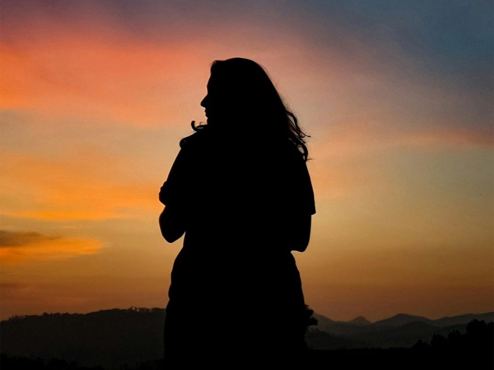 Silhouette of person meditating on a mountain top at sunset, symbolizing transition and reflection