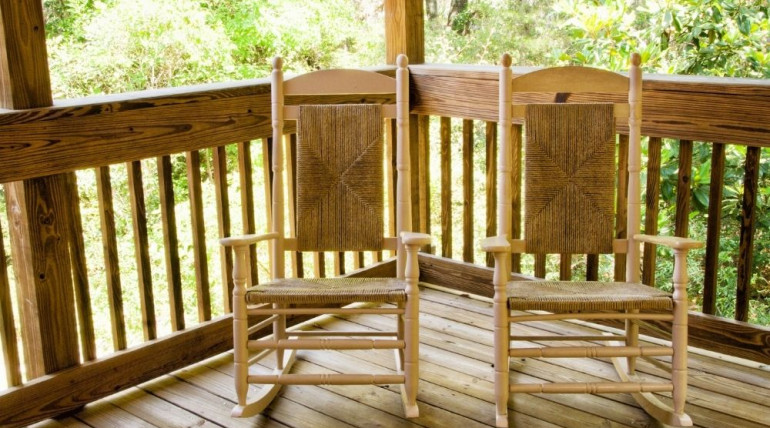 Two wooden rocking chairs on a porch overlooking the woods, symbolizing gentleness and shared retreat