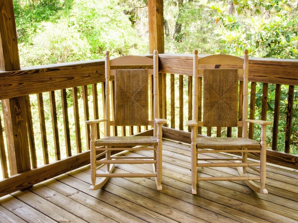 Two wooden rocking chairs on a porch overlooking the woods, symbolizing gentleness and shared retreat